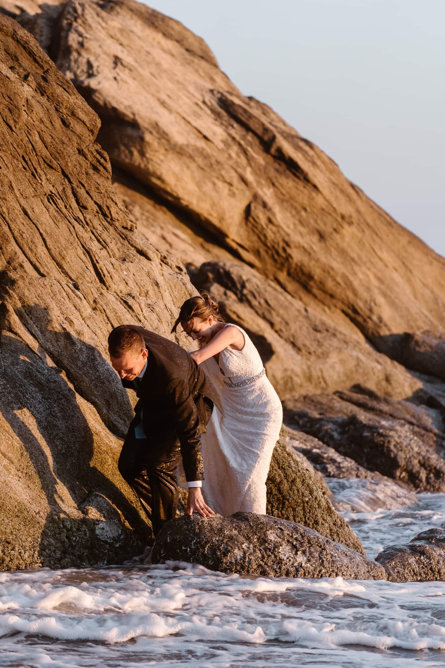 Bride and Groom climbing on rock at Hug Point & Cannon Beach Elopement