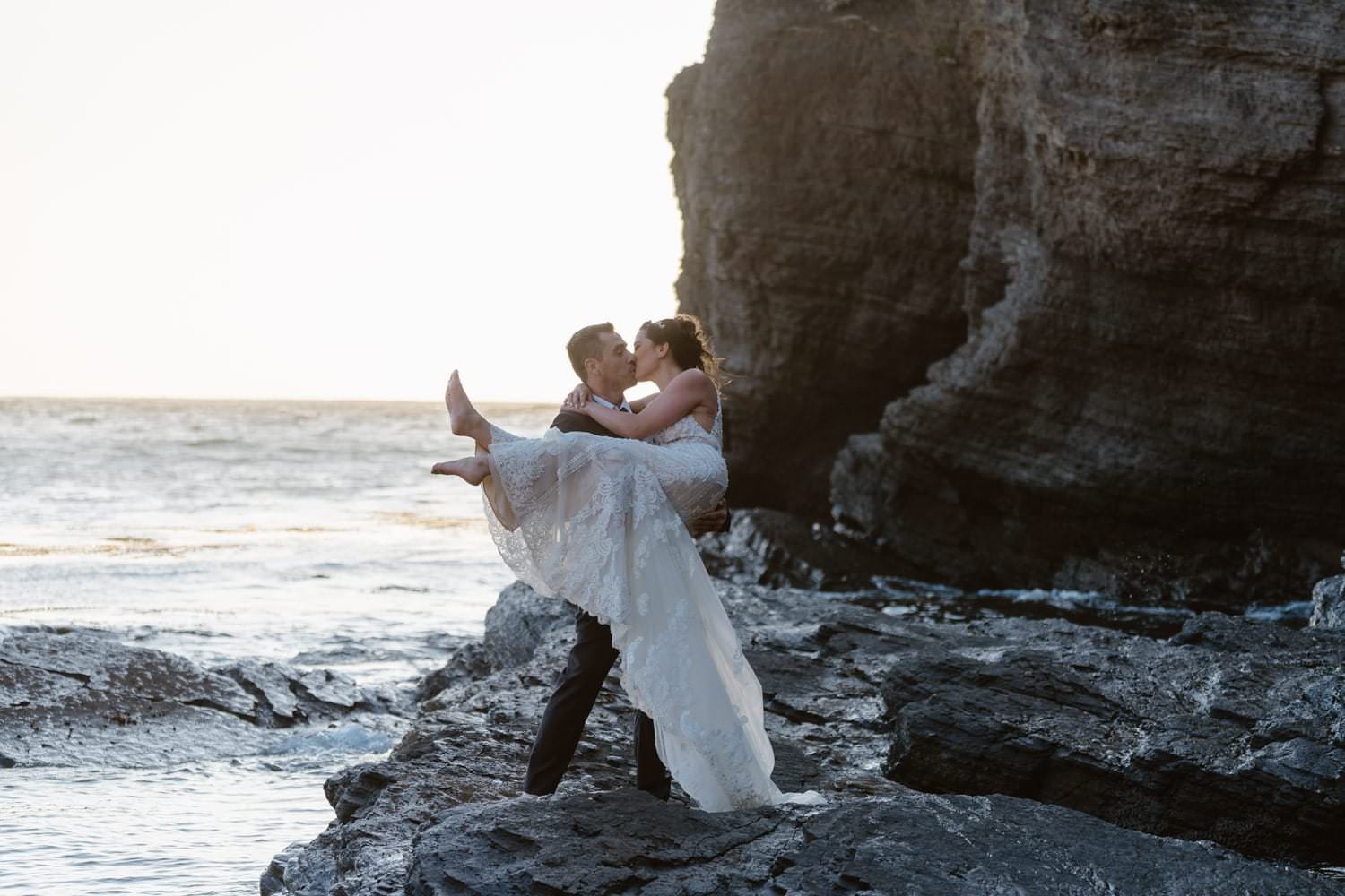 Groom holding bride on rock at the ocean at Big Sur Elopement