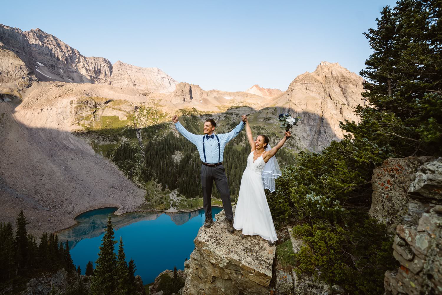 A bride and groom throwing their hands up in celebration in the mountains of Colorado.