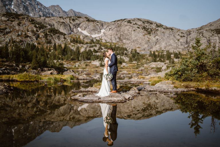 Bride and groom share kiss with reflections coming off alpine lake for their Colorado elopement.