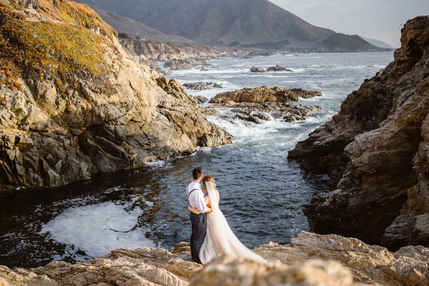 Bride and groom sharing a hug overlooking the ocean in Big Sur.
