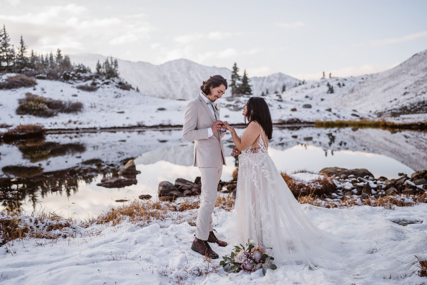 A groom putting the ring on his bride in the snowy Colorado mountains.