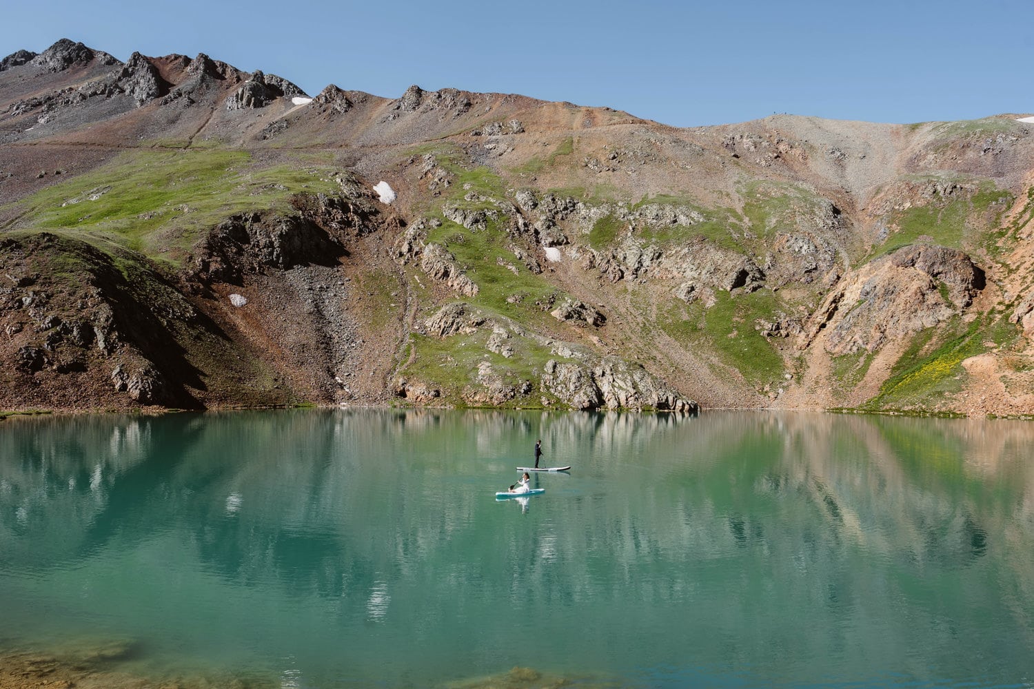 A bride and groom paddle boarding on an alpine lake in the San Juan mountains.