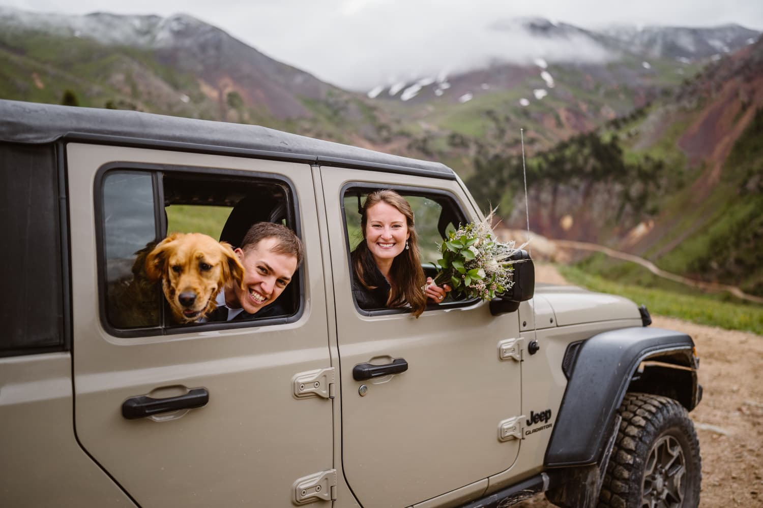 A bride, groom and their dog in a jeep on their wedding day.