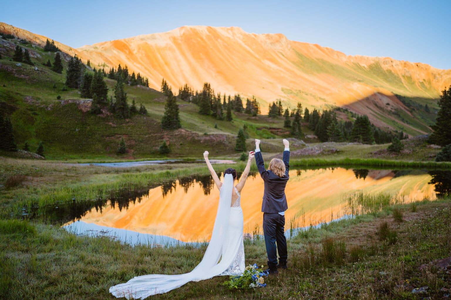 A couple celebrating their elopement near an alpine lake reflection in Colorado.