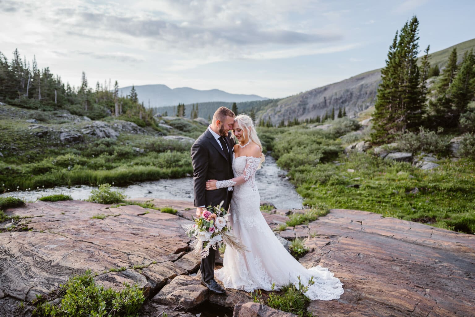 A bride and groom sharing a laugh on their elopement near a waterfall at sunrise in Colorado.