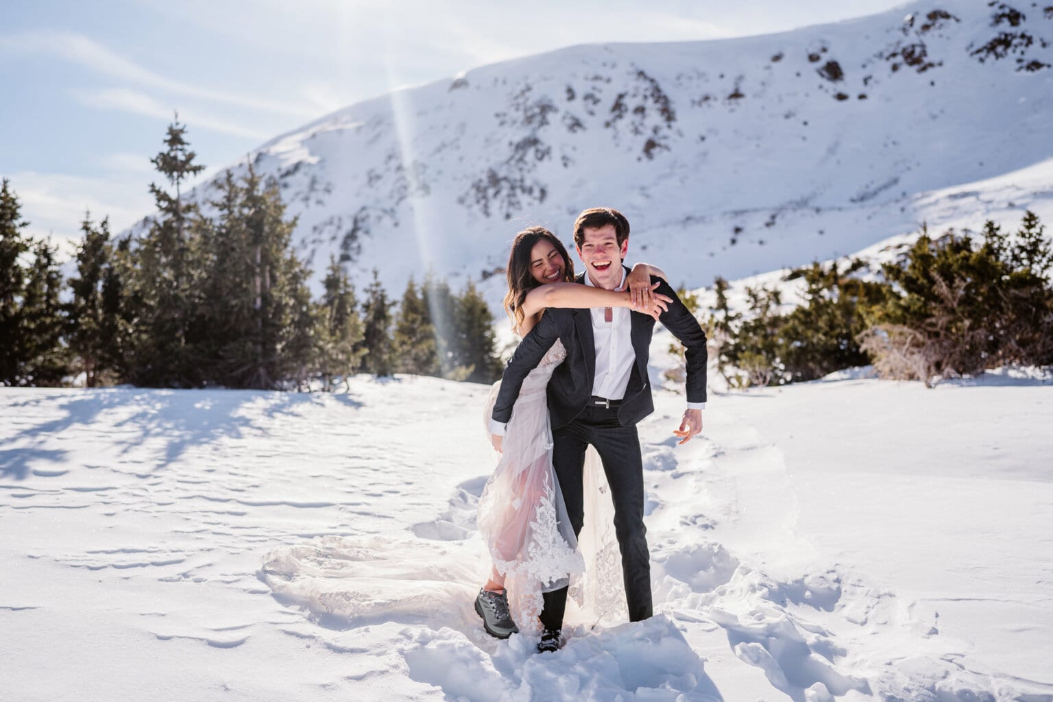 Bride jumping on her grooms back while dancing in the snow on their elopement day.