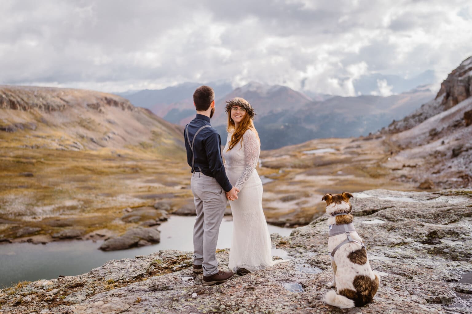 A couple standing on a ridge overlooking the mountains of Colorado with their dog on their elopement.