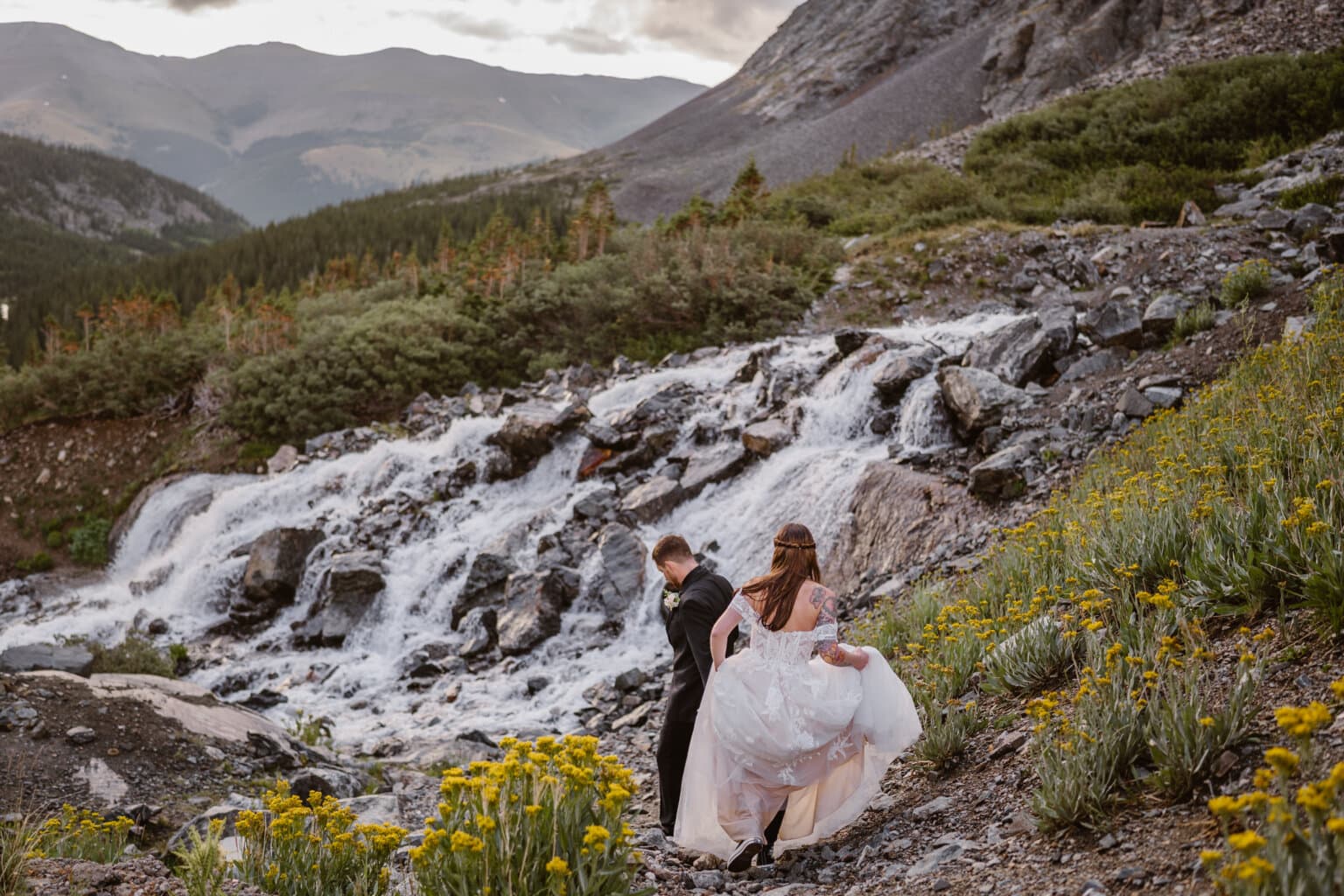 A couple hiking down some rocks towards a waterfall in Colorado on their elopement day.