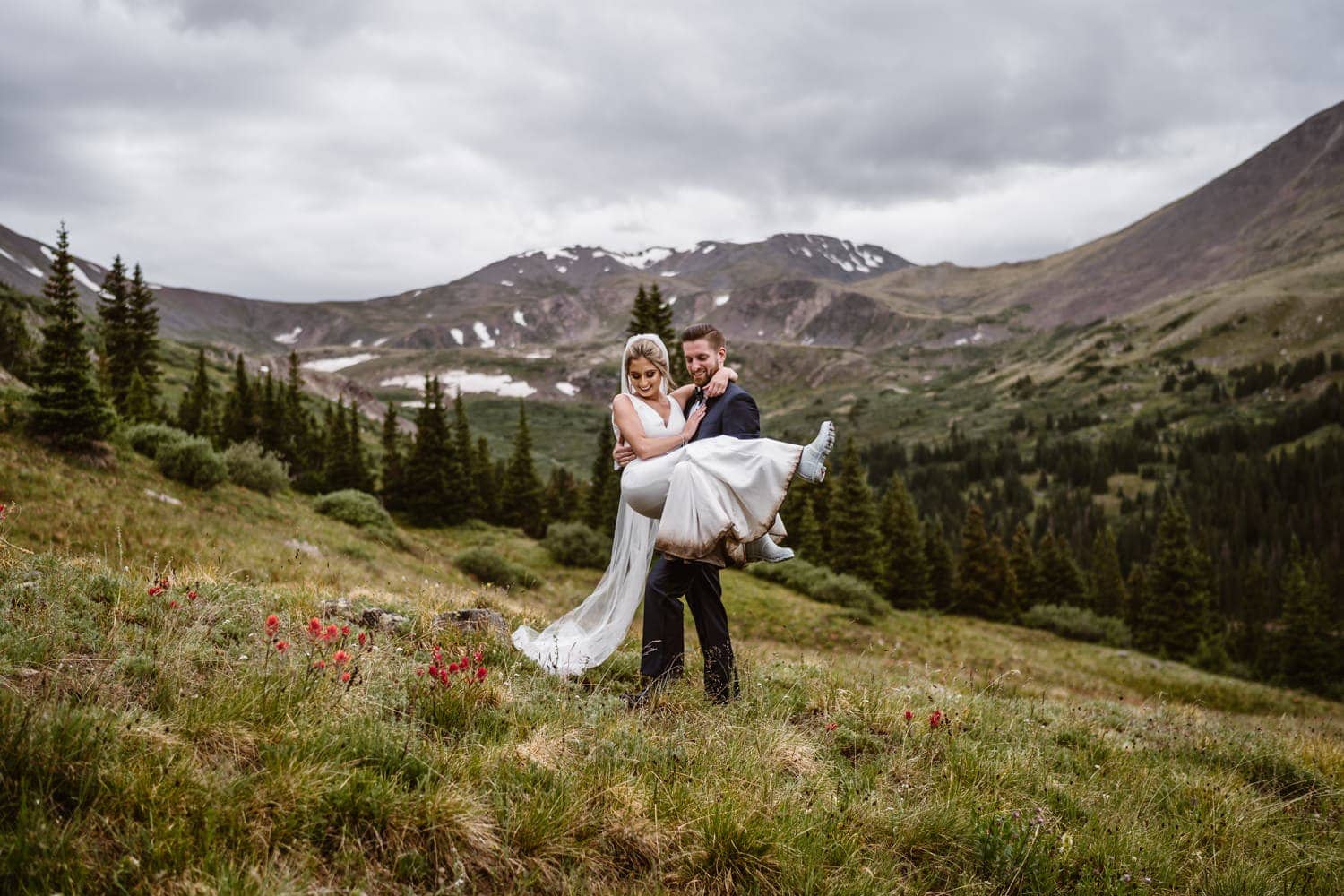 Groom carrying wife in his arms surrounded by the mountains.