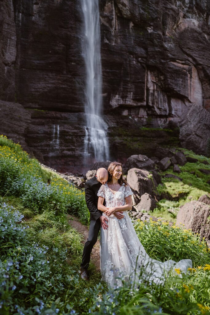 A couple standing near the flowers by a waterfall in Telluride for their elopement. 