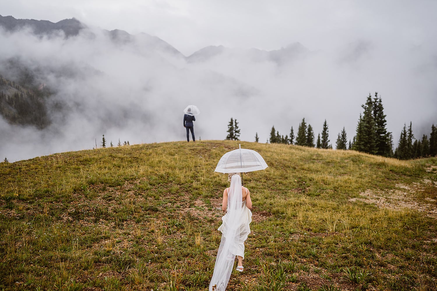 Bride walking out in the rain under an umbrella to do a first look with her husband in Colorado.