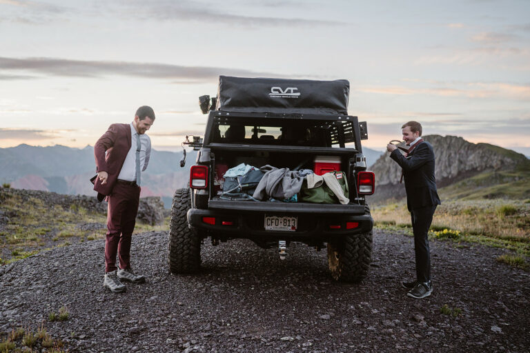 Two grooms getting ready for a first look near a jeep on a mountain pass for their Colorado elopement.