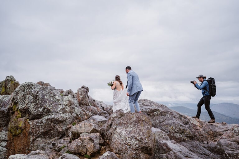 Couple hiking over some rocks with their videographer following behind them at their Colorado elopement.