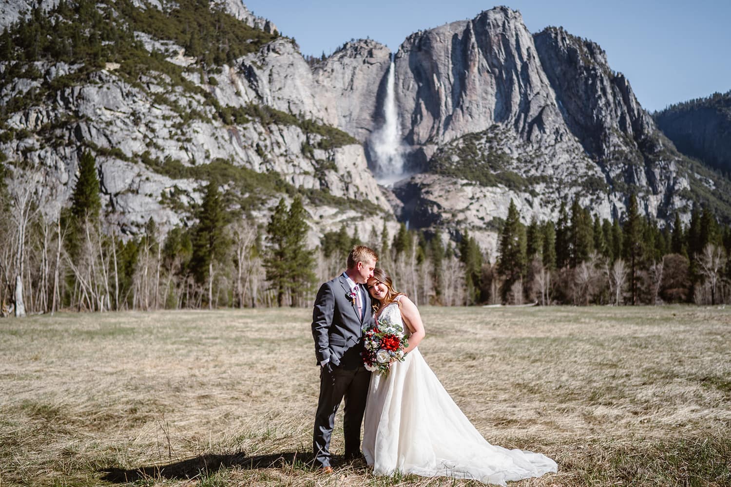 Couple standing in a field with Yosemite falls behind them on their elopement day in Yosemite.
